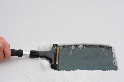 hand with an ice scraper cleaning a windshield