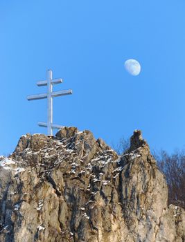 A cross on the top of the rock and a moon in background