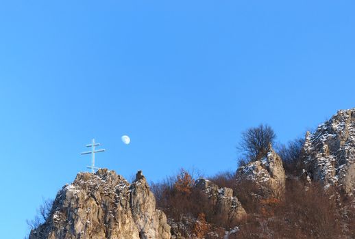 A cross on the top of the rock and a moon in background