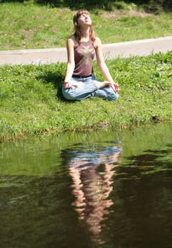 beautiful girl is meditating near by water with reflections