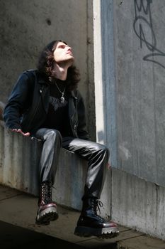 man in black leather cloth sits amongst concrete gray surfaces