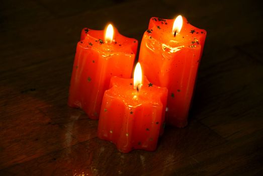 three orange burning star shape candles on dark wooden background