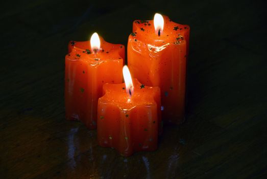 three orange burning star shape candles on dark wooden background