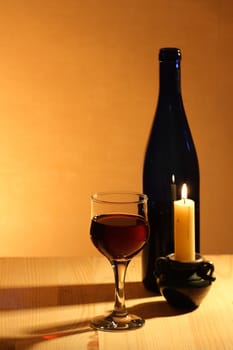 Wineglass near bottle of red wine and candle on nice brown background