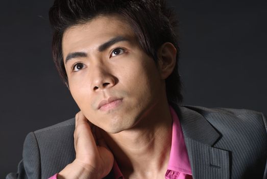 Handsome young businessman face, closeup portrait of Asian guy in studio in dark.