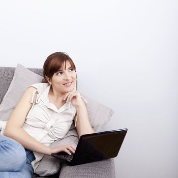 Beautiful woman seated on sofa with a laptop and thinking on something