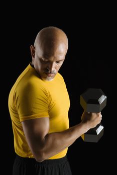 Mid adult multiethnic man wearing yellow exercise shirt doing arm curls while looking at bicep.