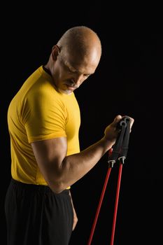 Mid adult multiethnic man wearing yellow exercise shirt exercising with stretch band and looking at bicep.