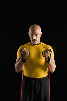 Mid adult multiethnic man wearing yellow exercise shirt exercising with stretch band while looking at viewer.