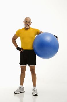 Mid adult multiethnic man standing and holding blue exercise ball looking at viewer.