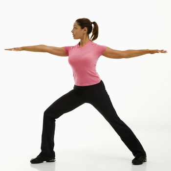 Side view of mid adult multiethnic woman wearing exercise clothing standing in yoga warrior pose.