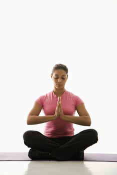 Mid adult multiethnic woman sitting in Namaste position on exercise mat with eyes closed and hands at heart center.