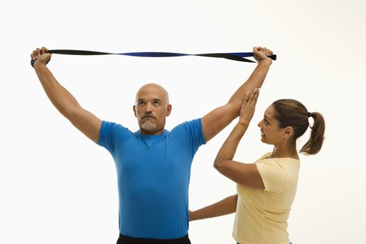 Mid adult multiethnic woman assisting mid adult multiethnic man with stretching band.