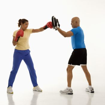 Mid adult multiethnic woman standing and punching focus mitts worn by multiethnic mid adult man.