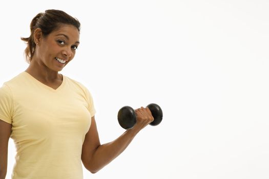 Mid adult multiethnic woman wearing yellow exercise shirt doing arm curls looking at viewer and smiling.