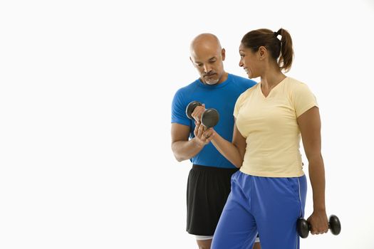 Smiling mid adult multiethnic man assisting mid adult multiethnic woman with dumbbells.