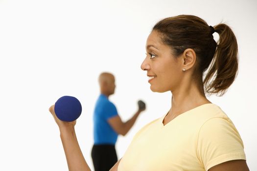 Close up of smiling mid adult multiethnic woman exercising using dumbbells with mid adult multiethnic man in background.