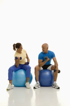 Mid adult multiethnic man and woman balancing on blue exercise balls while working out with dumbbells.