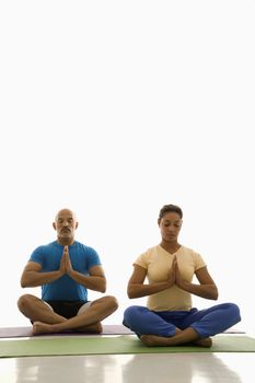 Mid adult multiethnic man and woman sitting in Namaste position on exercise mats with eyes closed and hands at heart center.