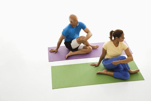 Mid adult multiethnic man and woman sitting and stretching on exercise mats.