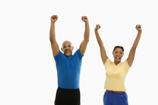 Enthusiastic mid adult multiethnic man and woman wearing exercise clothing with arms stretched overhead in excitement.