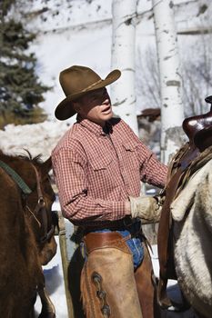 Caucasian male wrangler putting saddle on horse.