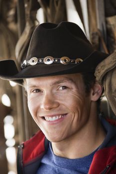 Young adult Caucasian male wearing cowboy hat smiling at viewer.