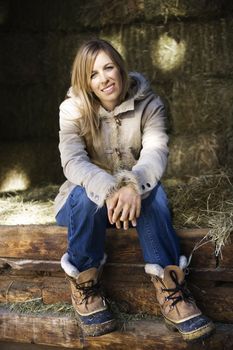 Young adult Caucasian woman sitting in barn with hay smiling at viewer.