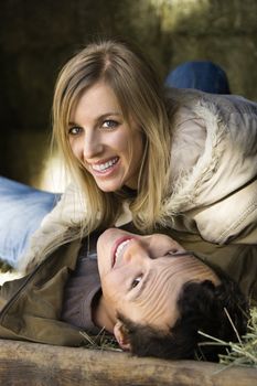 Young adult Caucasian couple lying in hay and smiling up at viewer.