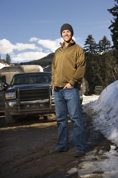 Young Caucasian man standing in front of truck with hands in pockets smiling at viewer.