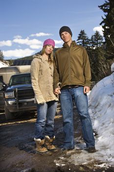 Young Caucasian couple holding hands looking at viewer with truck in background.