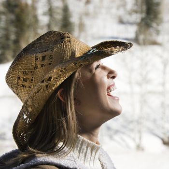 Young Caucasian woman laughing wearing cowboy hat outdoors in winter.