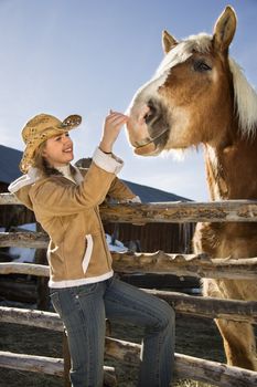 Young Caucasian woman leaning on fence petting horse.