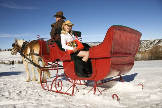 Young adult Caucasian woman holding present and mid-adult man in horse-drawn sleigh.