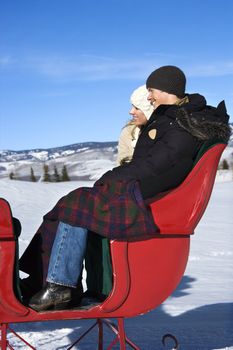 Side view of happy young Caucasian couple seated in sleigh.