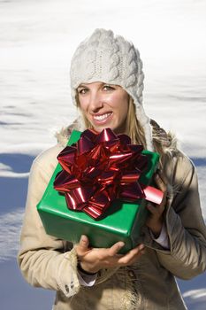Young adult Caucasian woman outdoors in winter attire holding present.