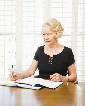 Mature Caucasian woman writing in calendar.