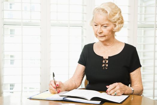 Mature Caucasian woman writing in calendar.