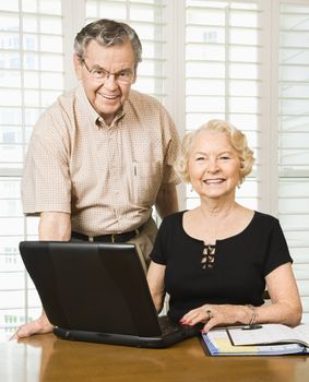 Mature Caucasian couple looking at their calendar and using laptop.