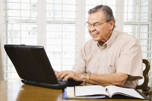 Mature Caucasian man typing on laptop in home.