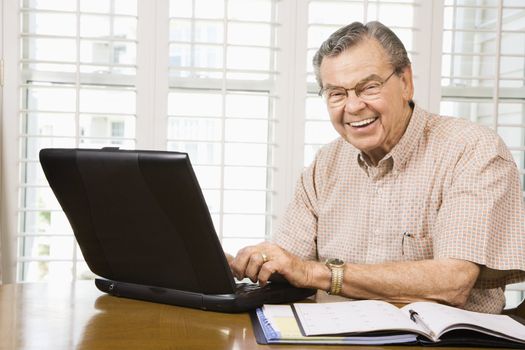 Mature Caucasian man typing on laptop in home.