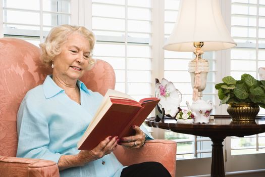 Mature Caucasian woman sitting in chair reading a book.