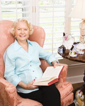 Mature Caucasian woman sitting in chair reading a book.