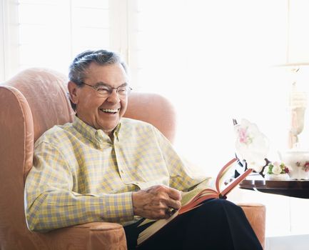 Mature Caucasian man sitting in chair reading a book.