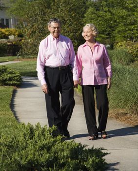 Mature Caucasian couple walking down sidewalk.