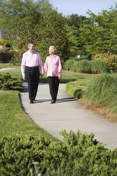Mature Caucasian couple walking down sidewalk.