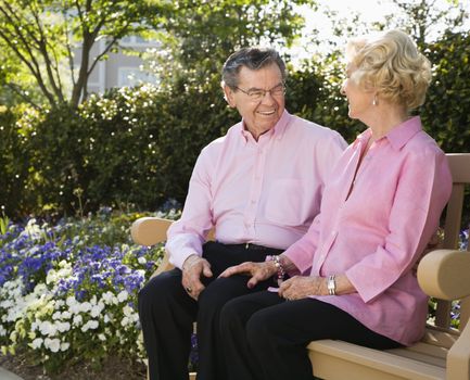 Mature Caucasian couple sitting on bench looking at each other.