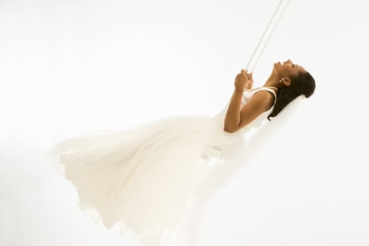 Mid-adult African-American bride swinging with white background.