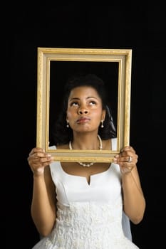 Mid-adult African-American bride holding frame around her face.