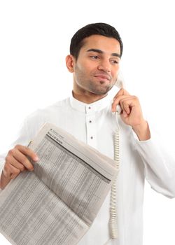 An ethnic mixed race man on a telephone call.  He is holding a newspaper and wearing traditional middle eastern clothing.  White background.